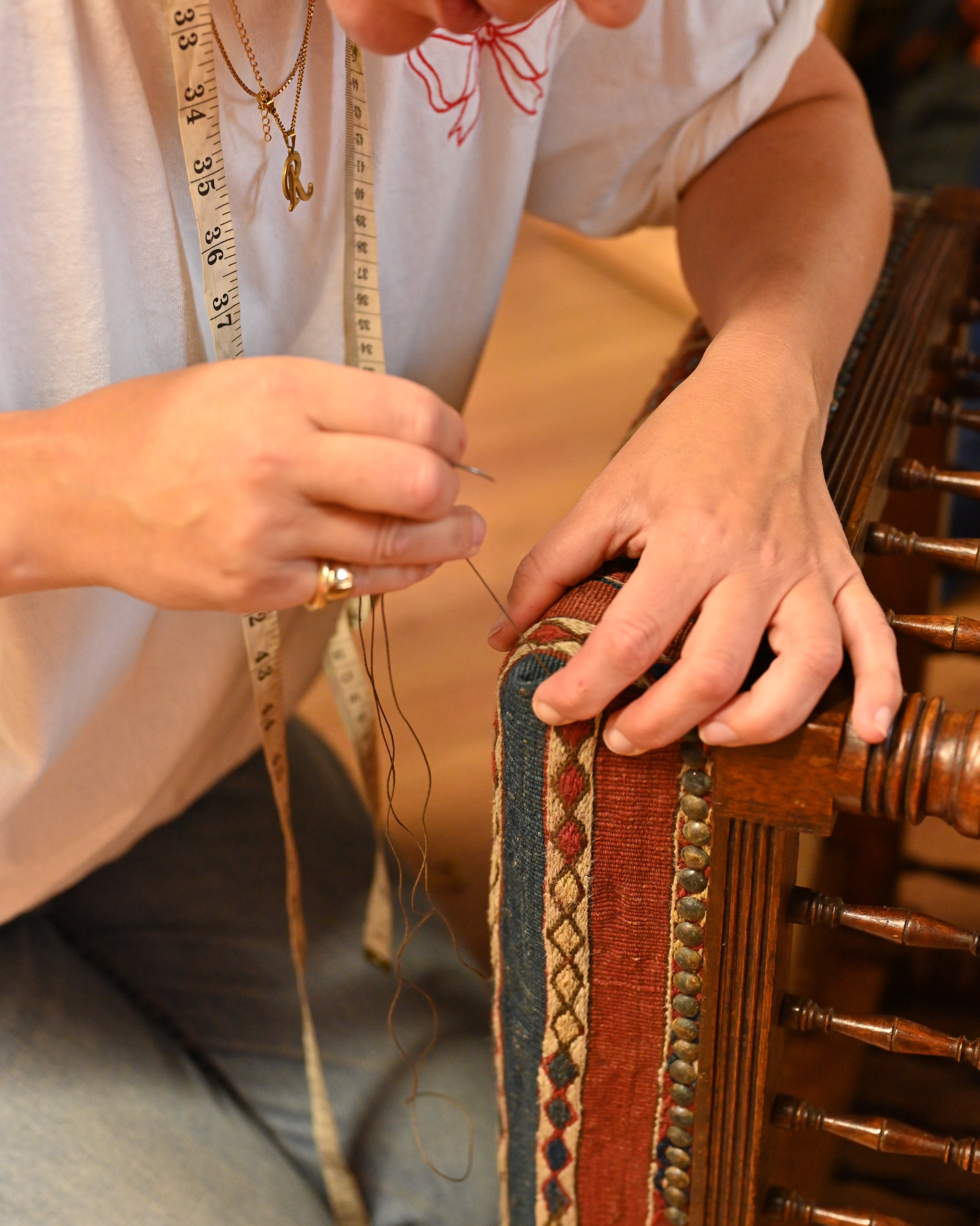 A female upholsterer photographed at work, up close and in portraits, in her studio, filled with wooden furniture, colorful fabric rolls, and mockup designs, and illuminated by bright light.