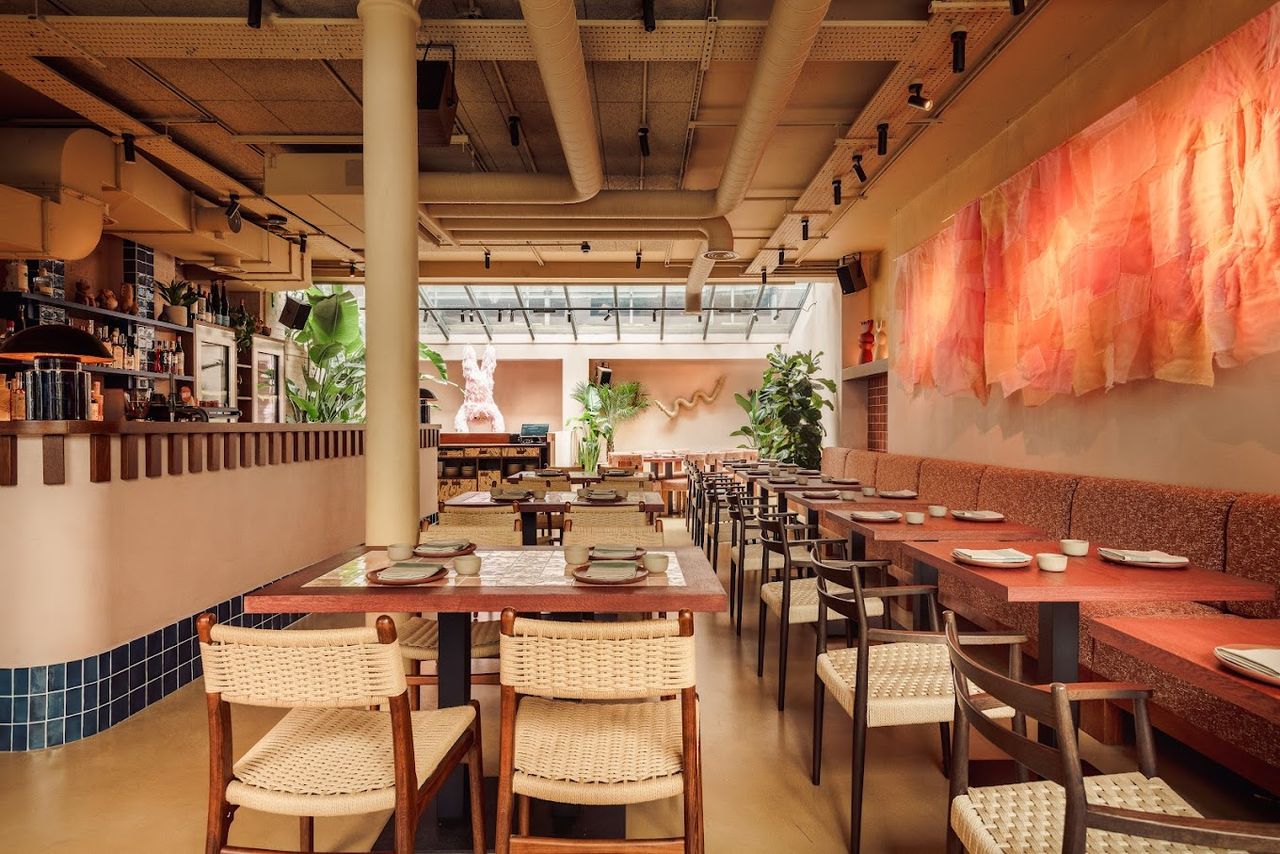 A warmly lit restaurant decorated with terracotta tiles, sculptural artworks, and wood and rattan furniture boasts an intimate atmosphere.