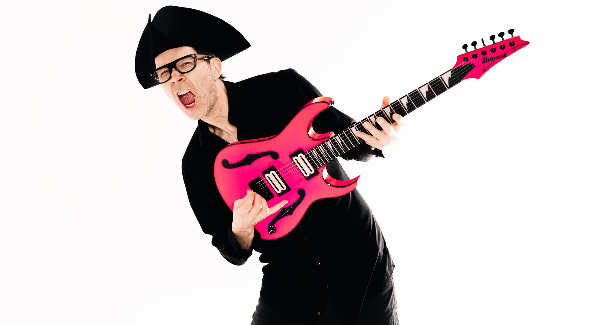 Paul Gilbert is dressed in all black &amp;ndash; and wears a tricorn hat &amp;ndash; as he poses with his pink Ibanez signature guitar.