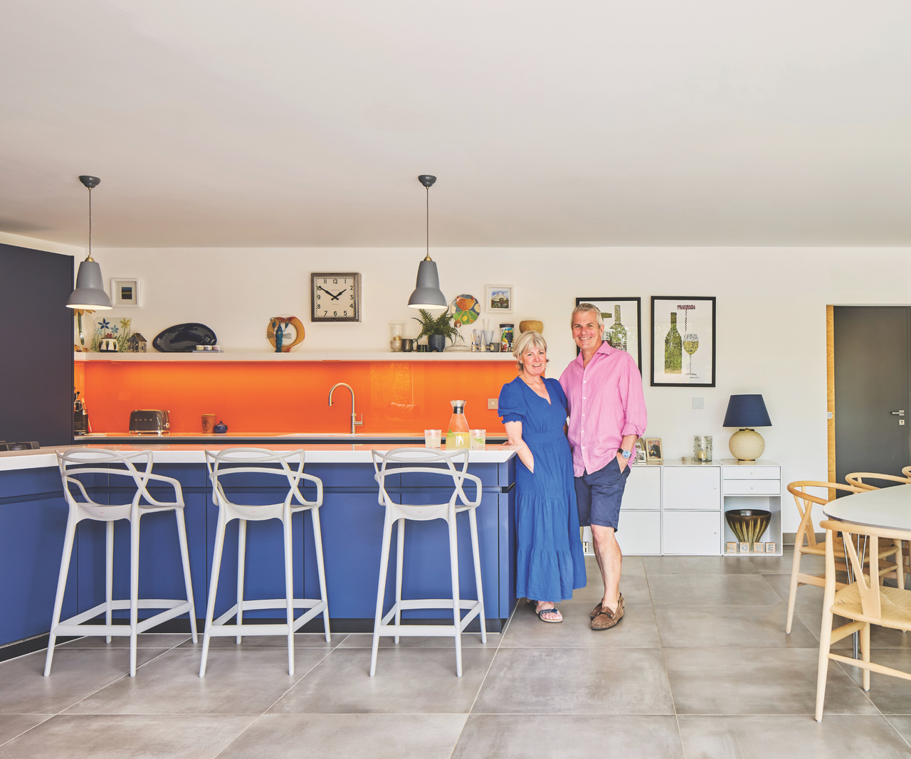 Kitchen with grey floor tiles, blue cabinets and orange backsplash, with couple standing beside the cabinets