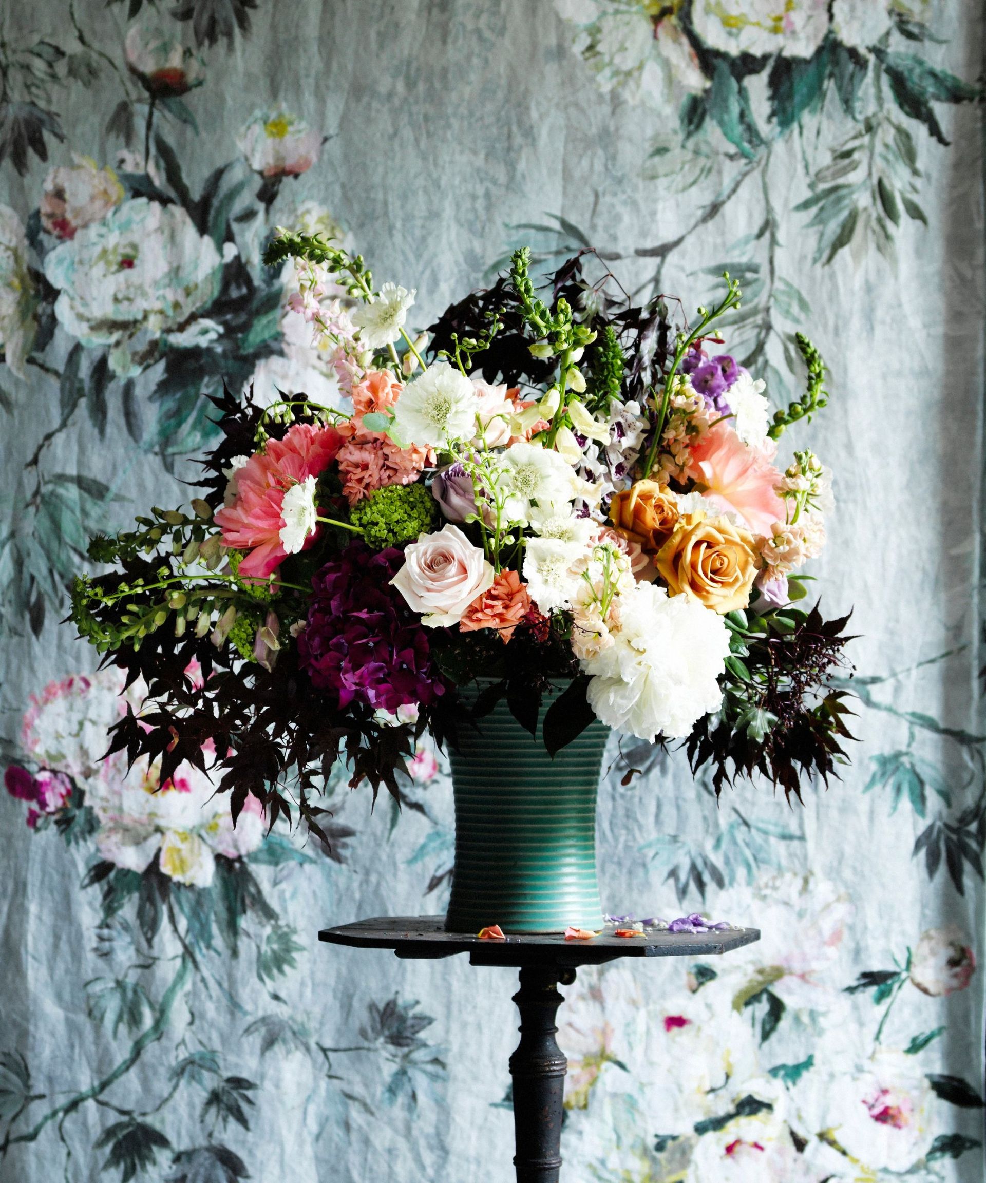 colorful flower arrangement on a pedestal with floral fabric hanging behind