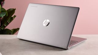 Back of opened lid of HP Chromebook Plus 15.6-inch on table with pink wall and plant in background