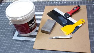 A tub of gesso next to a board and scraping tools