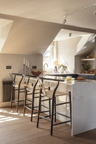 An eaves kitchen with sloping roof, bar stools at the counter and painted in Stone Hearty by Benjamin Moore