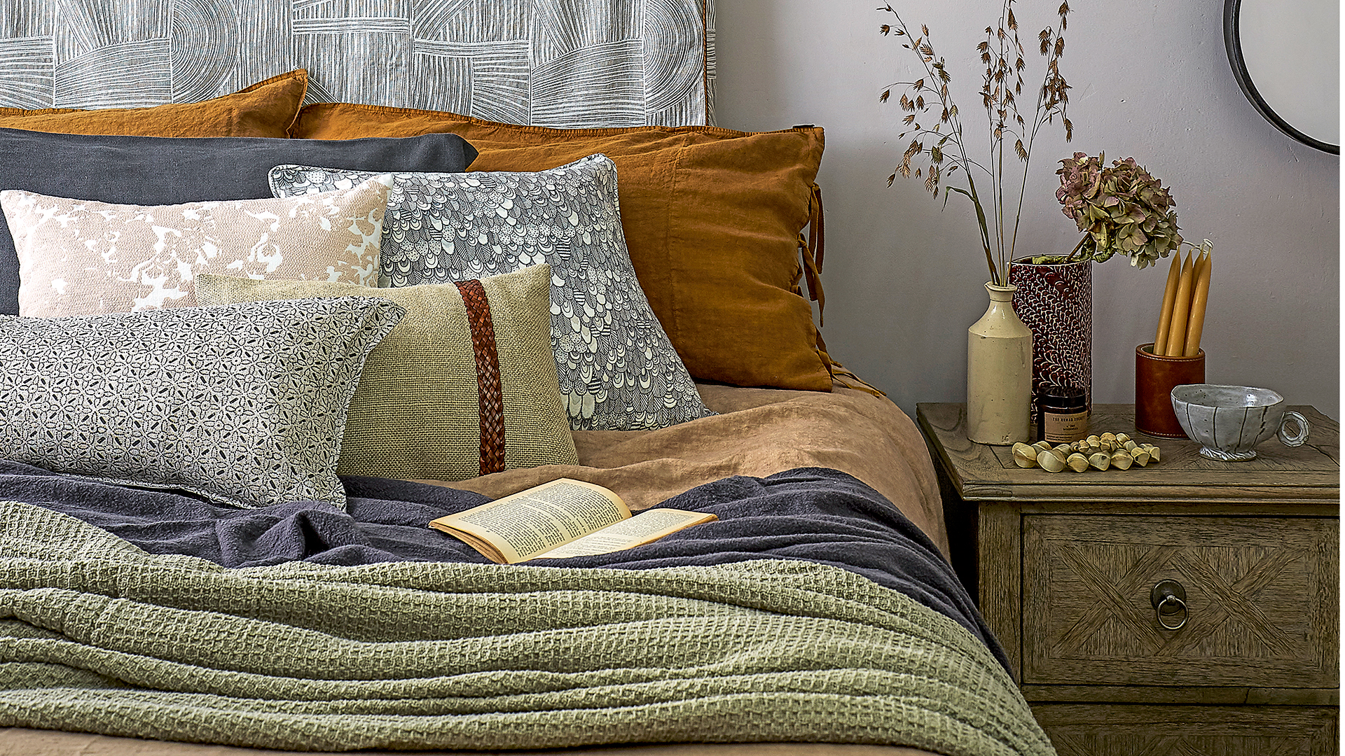 Bed layered with inviting cosy cushions and throws in rich autumn colours
