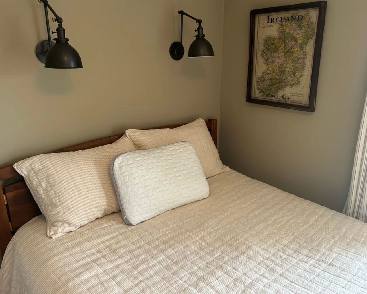 A Luxome LAYR pillow photographed on a double bed with a quilted bedspread with two black lights above and a map print of Ireland to the right.