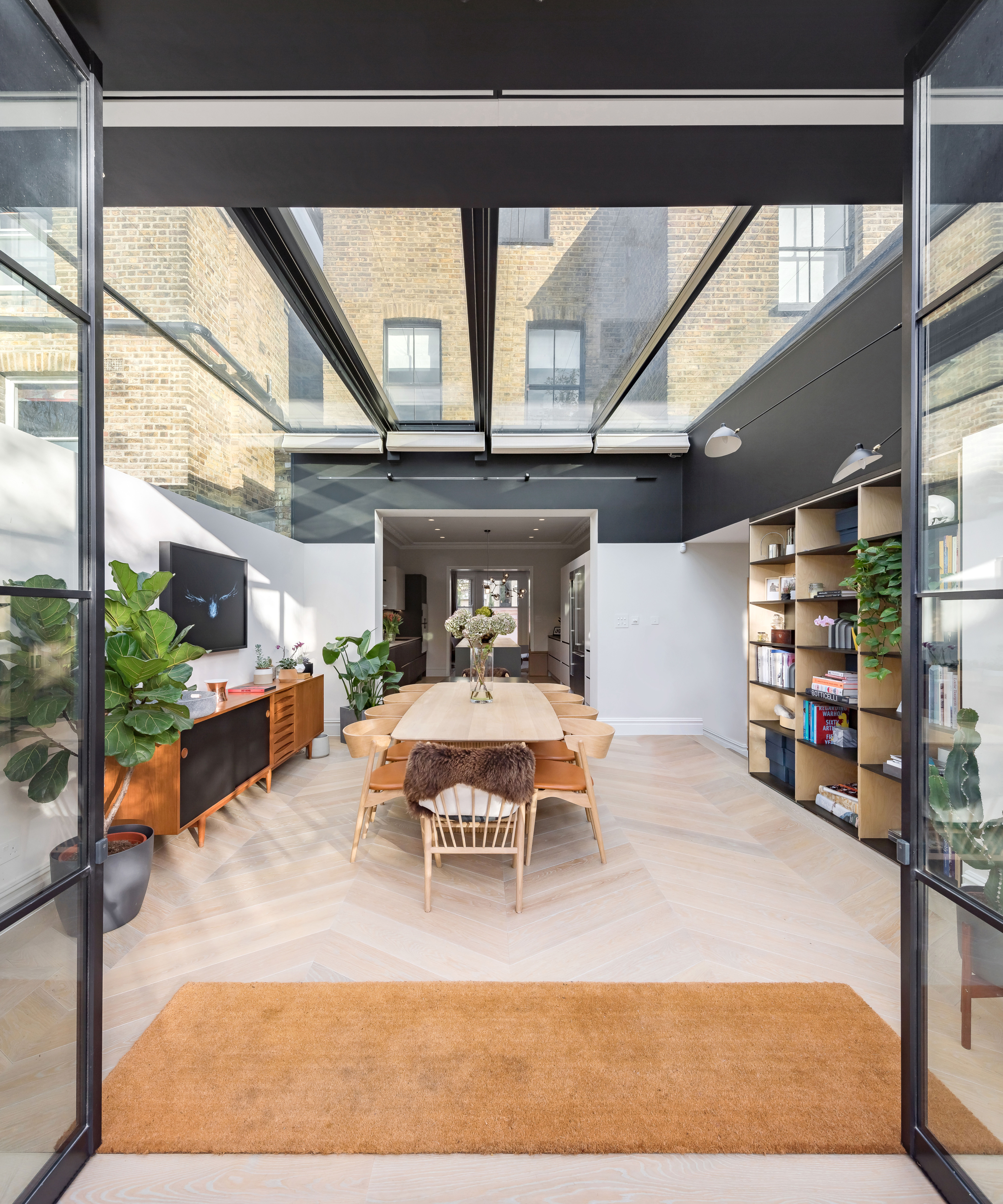 glass extension with glass roof and celestory windows but walls below, space used as dining room with wooden floor and built in display shelving