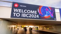 A large sign reading "Welcome to IBC 2024" above an underpass, with pedestrians walking beneath