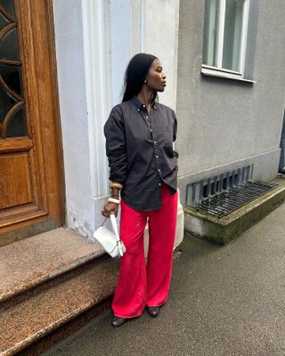 @nlmarilyn wearing a brown button-down shirt, white bag, and red silk pants.