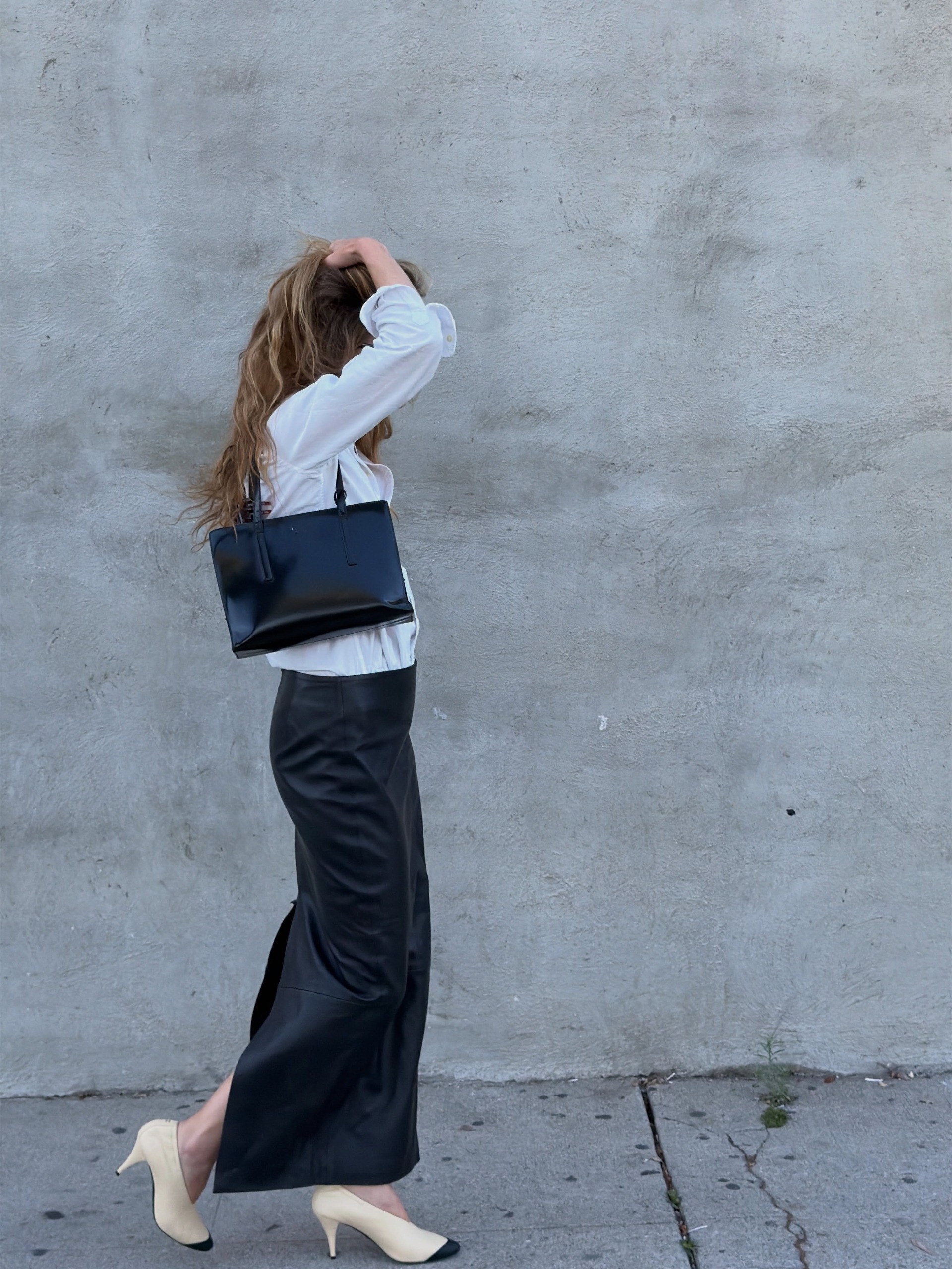 Eliza wears cap-toe heels, a black satin skirt, and a black bag.