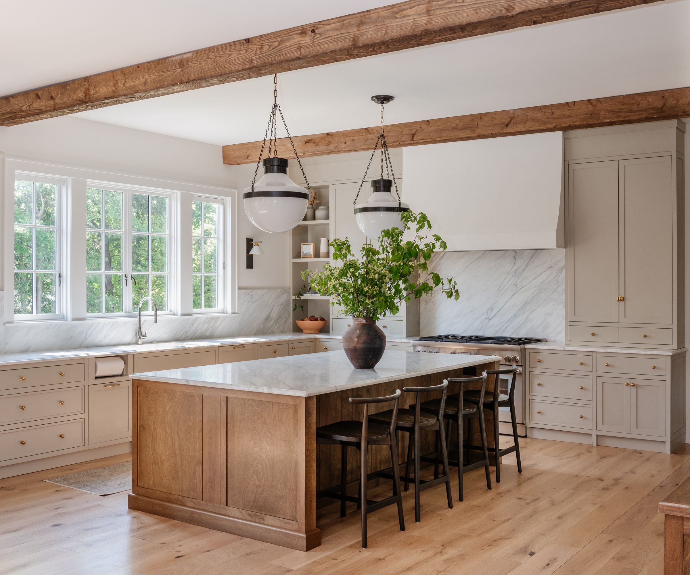 A large kitchen with warm white cabinets, a wooden island, and rustic wood ceiling beams