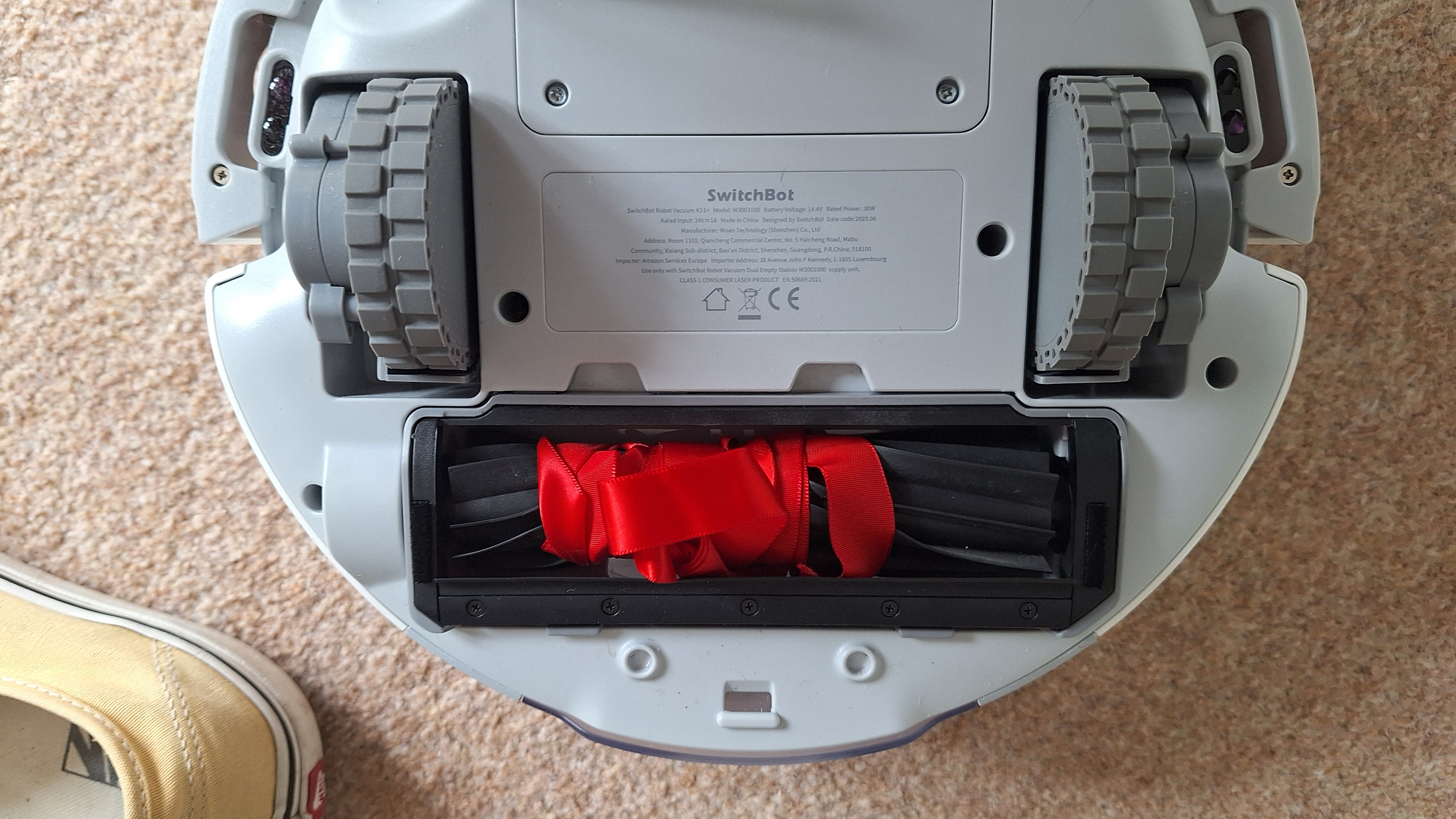 SwitchBot K11+ robot vacuum flipped over to show ribbon wrapped around roller