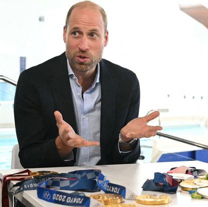 Prince William sitting at a table with Olympic medals and talking