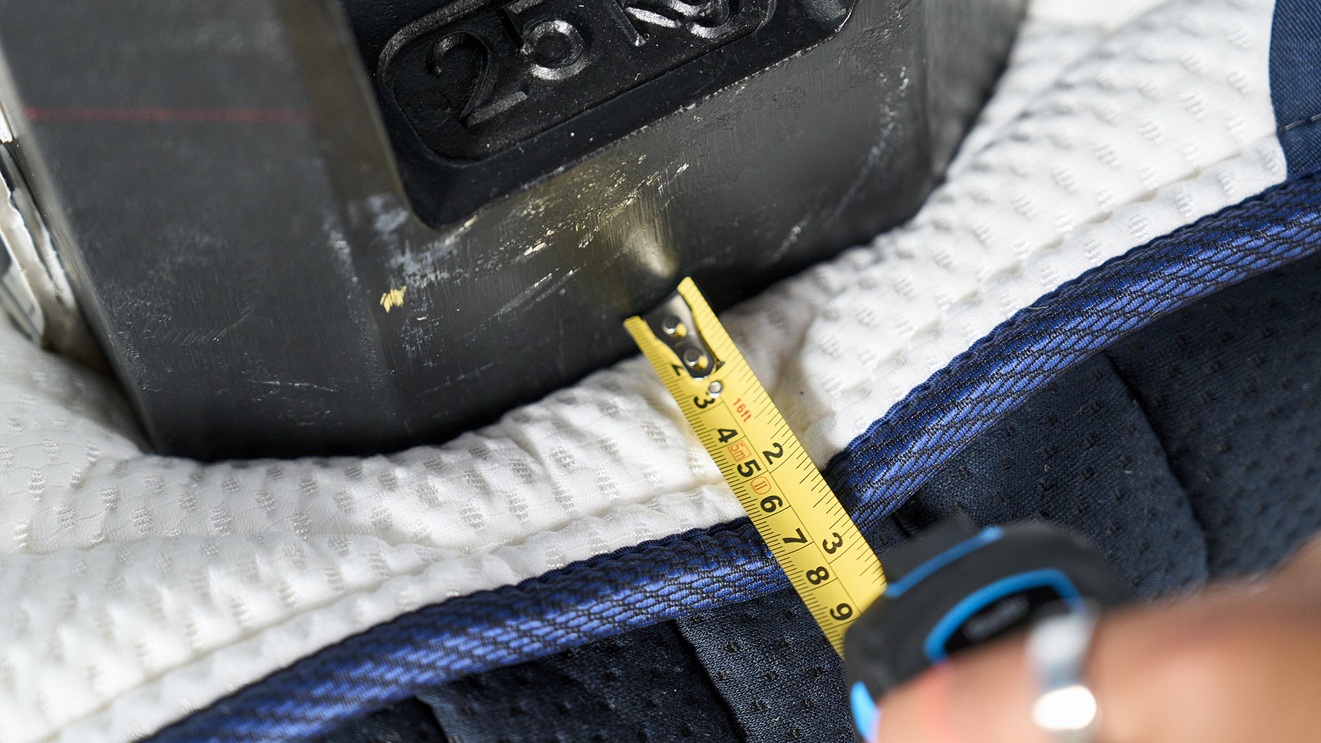 A close up of a measuring tape measuring 3" between the side of the DreamCloud Classic and the black 25kg weight