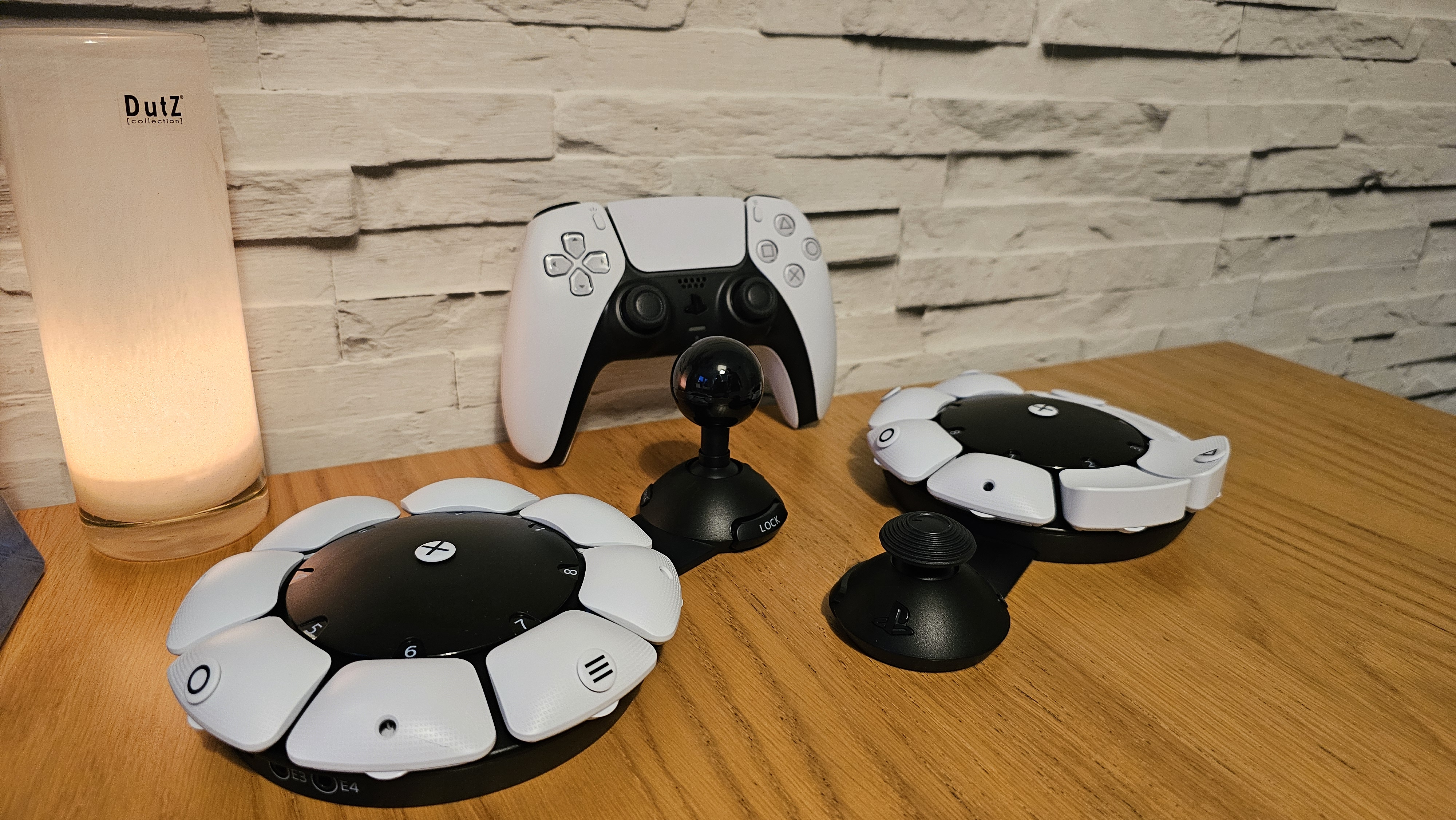 Two PlayStation Access controllers on a wooden surface with a DualSense controller