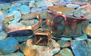 two chunky bangles, one with a long boulder opal and the other with a tall oval boulder opal, and a chunky ring with a square boulder opal, all three items displayed on a bed of boulder opal tiles