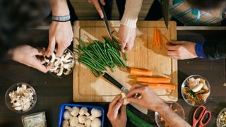 Group of hands cutting and chopping vegetables together on a worksurface
