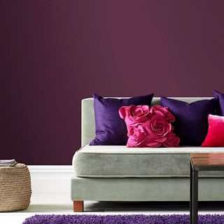 Purple painted wall behind grey sofa with purple and dark pink cushions