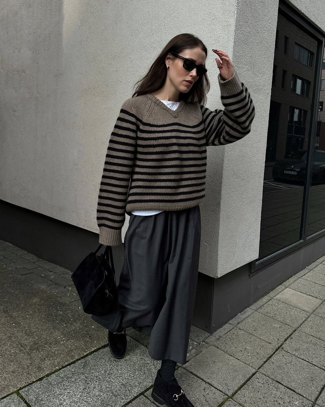 Content creator Annabel Rosendahl wearing a striped knit jumper, a grey skirt and black loafers. She has brown hair, and she's wearing black sunglasses too.