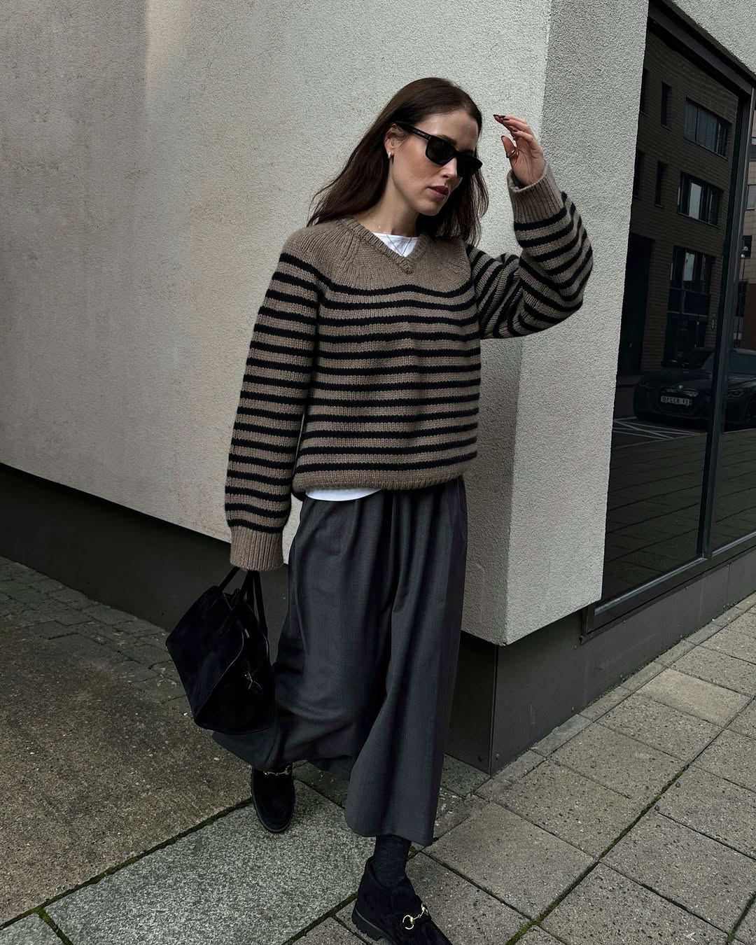 Content creator Annabel Rosendahl wearing a striped knit jumper, a grey skirt and black loafers. She has brown hair, and she&#039;s wearing black sunglasses too.