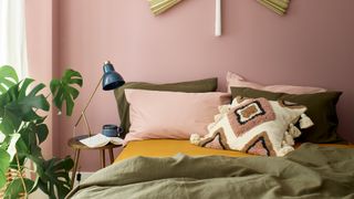 Pink bedroom paint color with Olive green bedding and houseplant