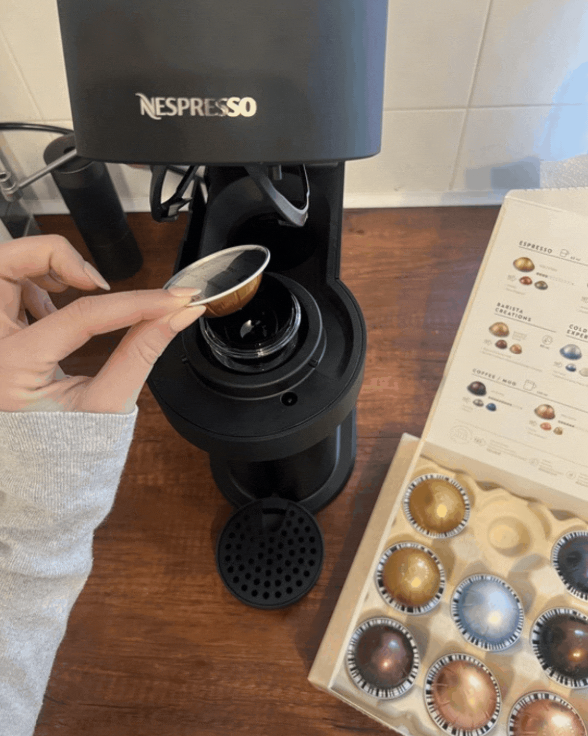 GIF of a hand putting a coffee pod into the Nespresso Vertuo Next machine on a wooden countertop.