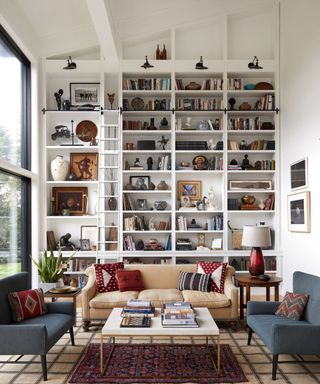 A living room with floor-to-ceiling white bookshelves full of books and decor, and a seating arrangement with vintage furniture