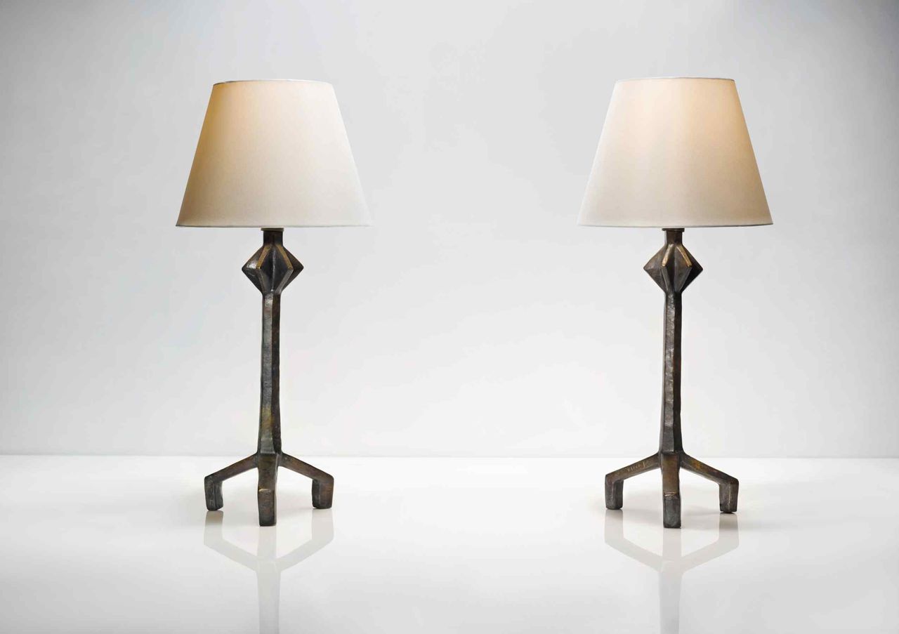 Two table lamps with white shades photographed on a white reflective surface against a white wall