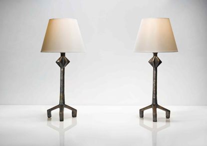 Two table lamps with white shades photographed on a white reflective surface against a white wall