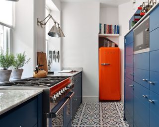 An example of how to plan a layout for a small kitchen showing a Neptune kitchen with blue cabinets, blue and white mosaic floor tiles and an orange refrigerator