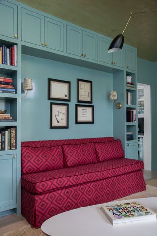 Red patterned upholstered bench with blue painted shelving at either side and above and coffee table