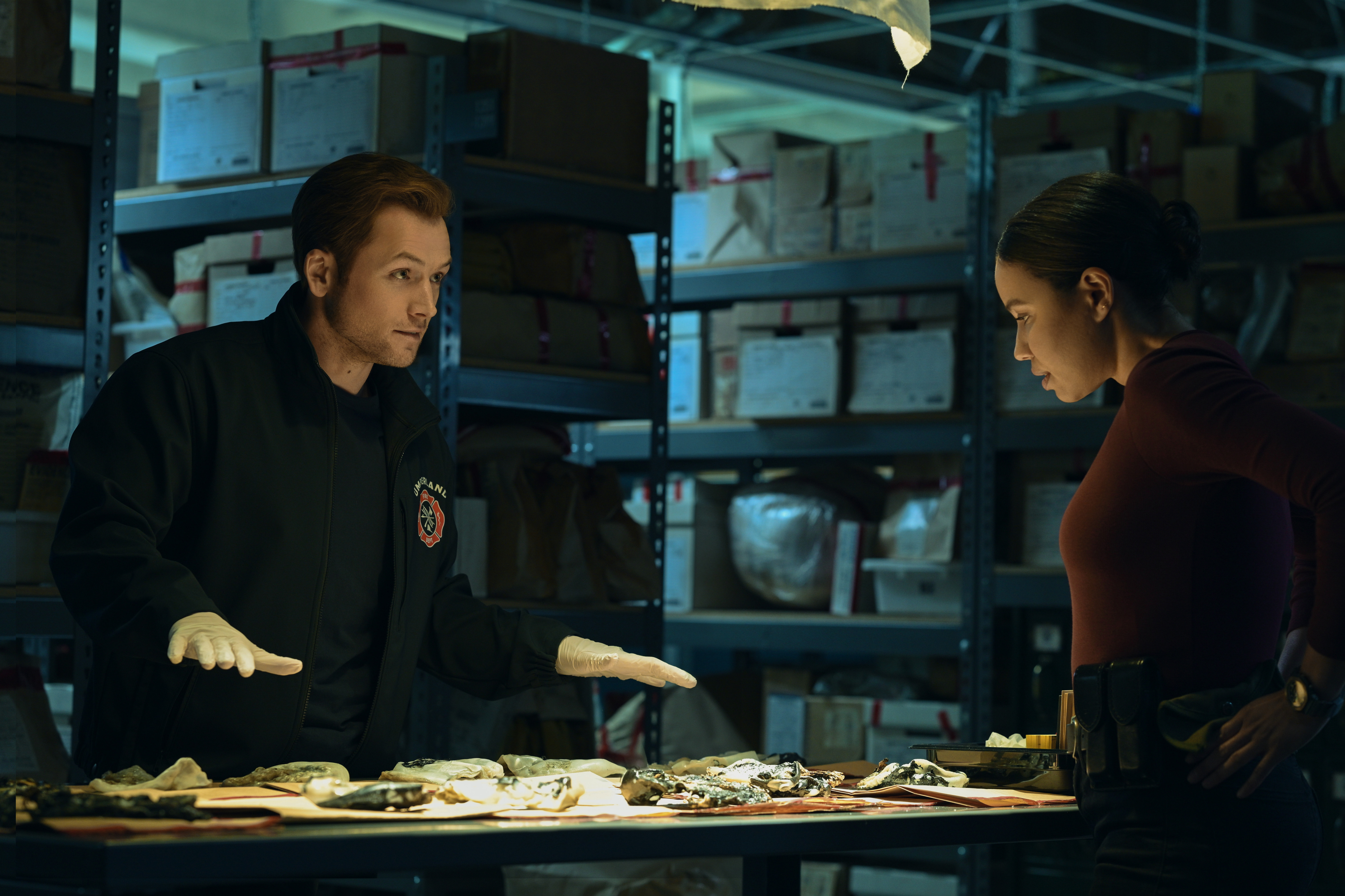 Taron Egerton and Jurnee Smollett as two investigators in the evidence room in smoke