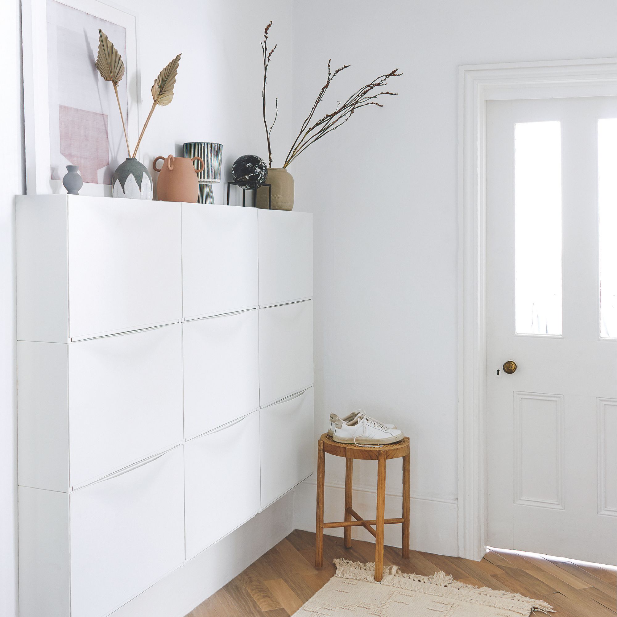 White painted hallway with white storage unit for shoes and brown wooden floors