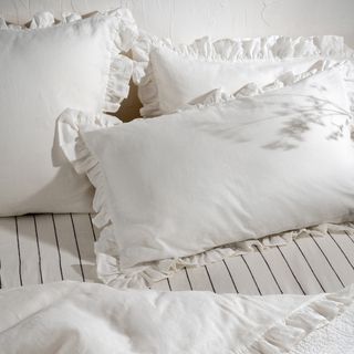 Three white linen pillowcase with a frill edge on a beige sheet with a black pinstripe