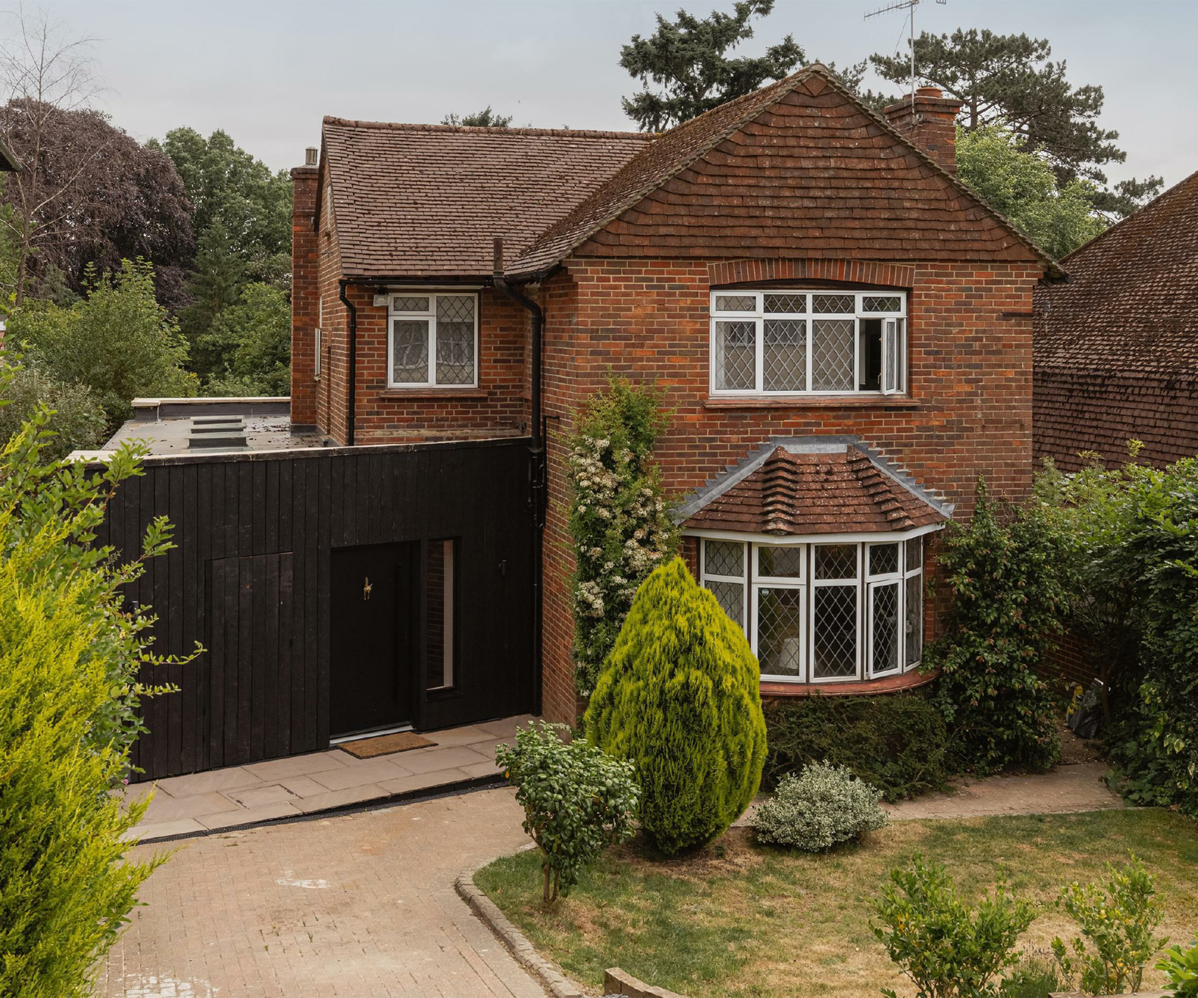 Exterior of a red brick home with contemporarynblack clad side extension