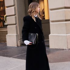 Nikki wears a black wool coat and white button-up with cashmere tights.