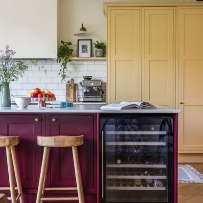 A kitchen with a burgundy-painted island and yellow cabinets on the wall