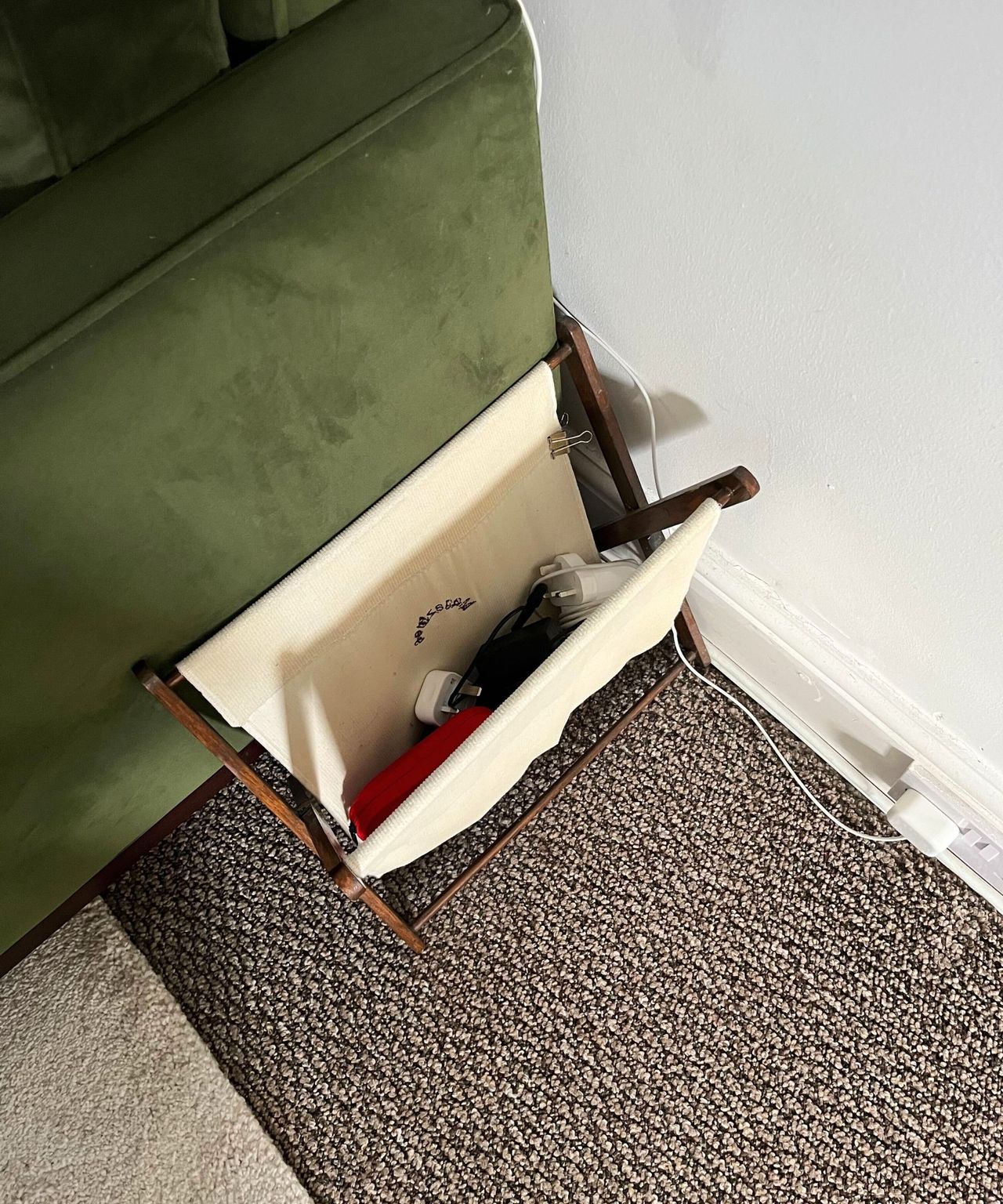 A magazine rack next to a green velvet couch with tidy cables inside.