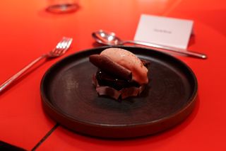 An ice cream dessert on a dark plate on a red table cloth in a dark room