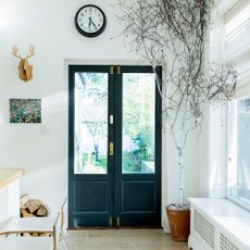 room with white wall black door indoor plant and clock