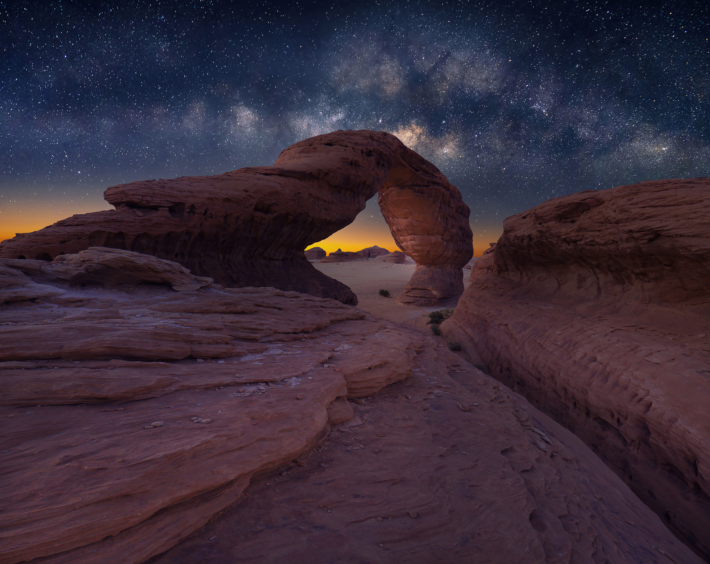 Starry night sky with the Milky Way stretches over a natural stone arch in a desert landscape