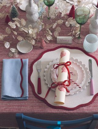 Christmas place setting with handmade cracker, candy cane, red and white tablecloth, honesty garland