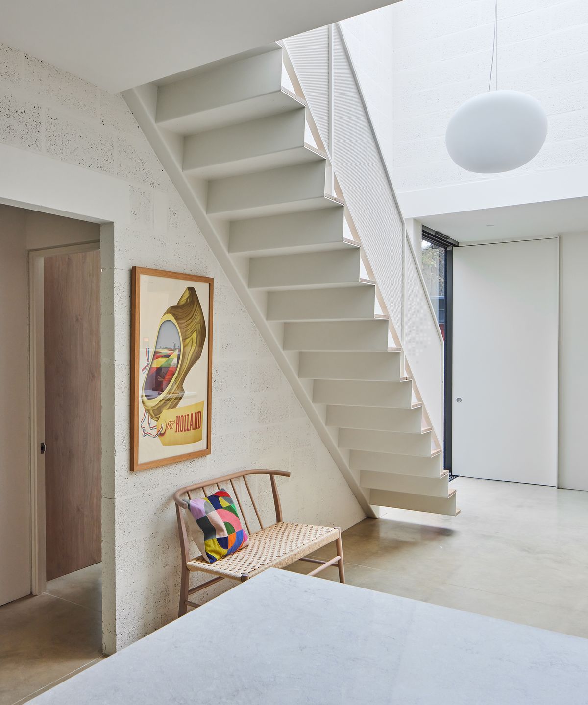 An open plan area underneath a new staircase with wooden bench seating and bright cushion underneath