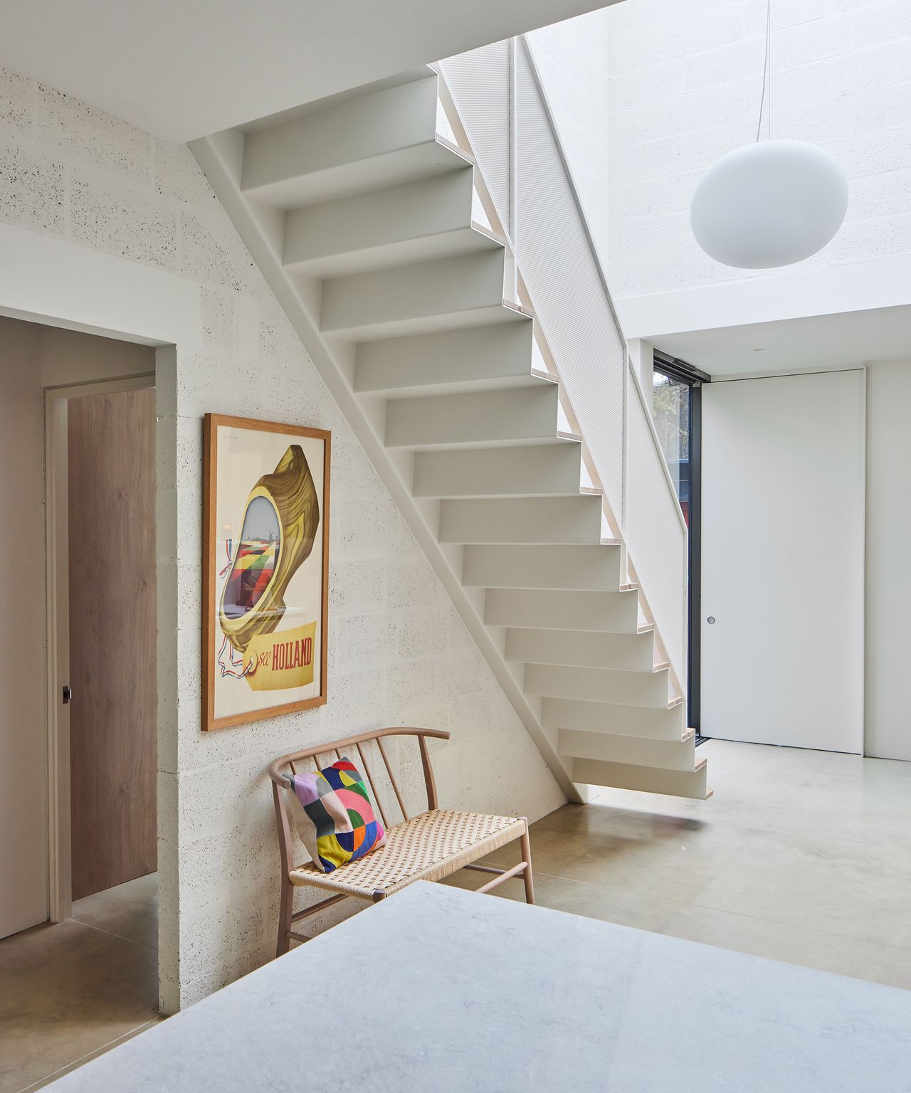 An open plan area underneath a new staircase with wooden bench seating and bright cushion underneath
