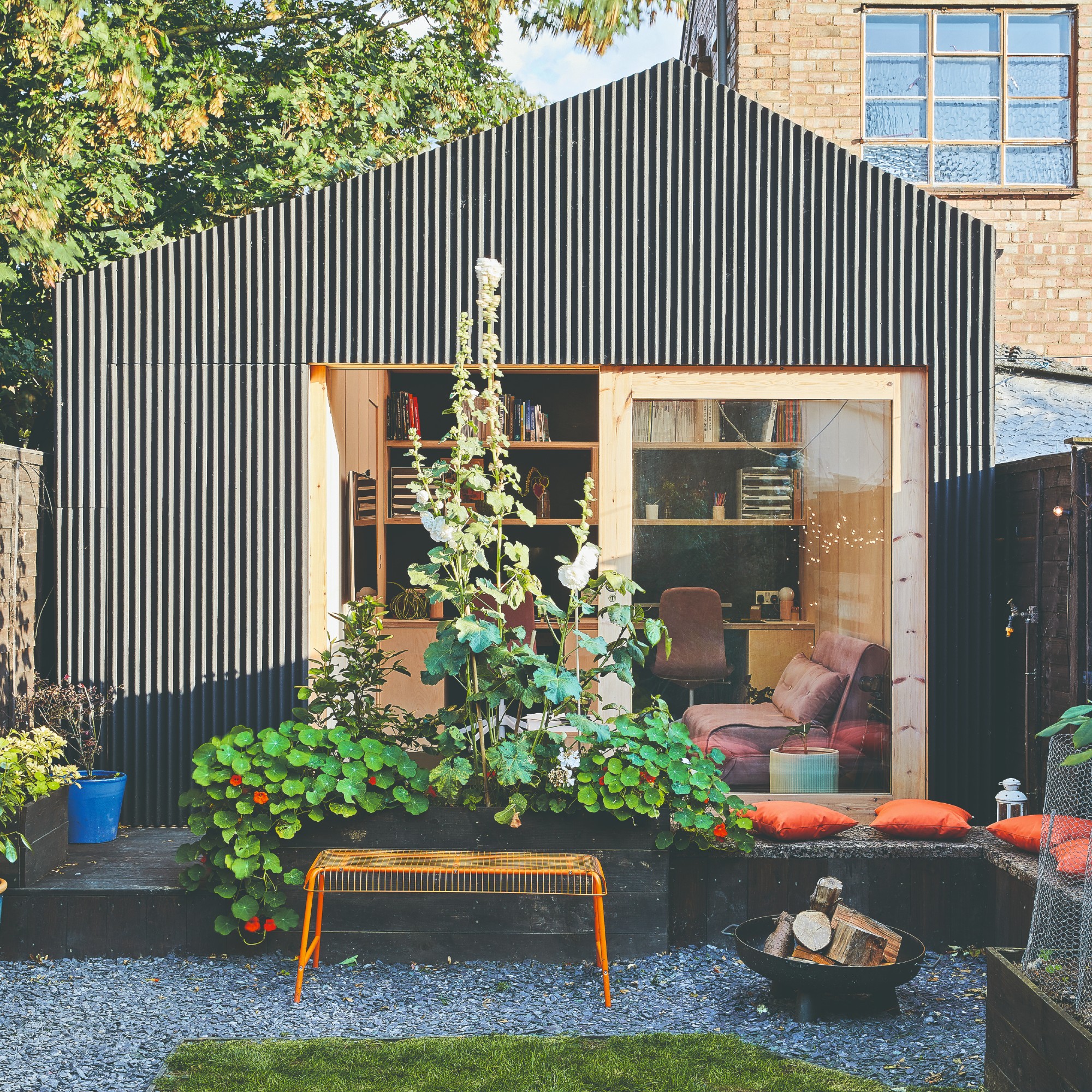 A garden with a fire pit and seating around it and an orange metal garden bench