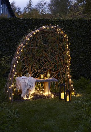 Outdoor solar arbour from Lights4fun set on the grass, with a dining set inside