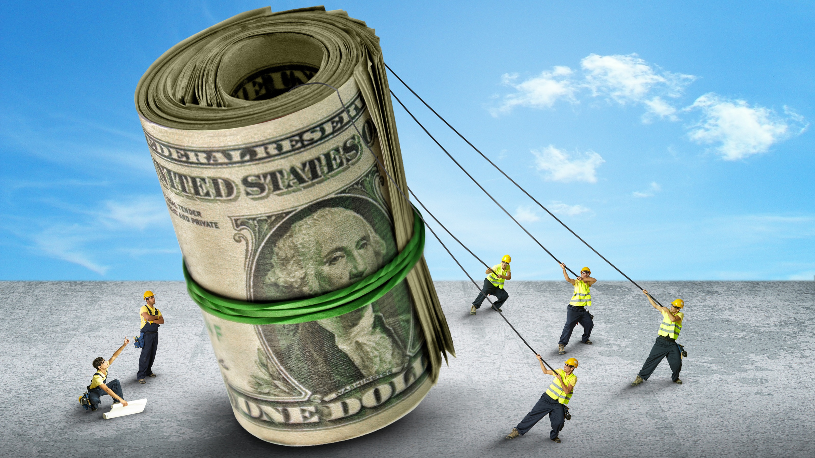 Tiny construction workers use ropes to hoist a roll of dollar bills.