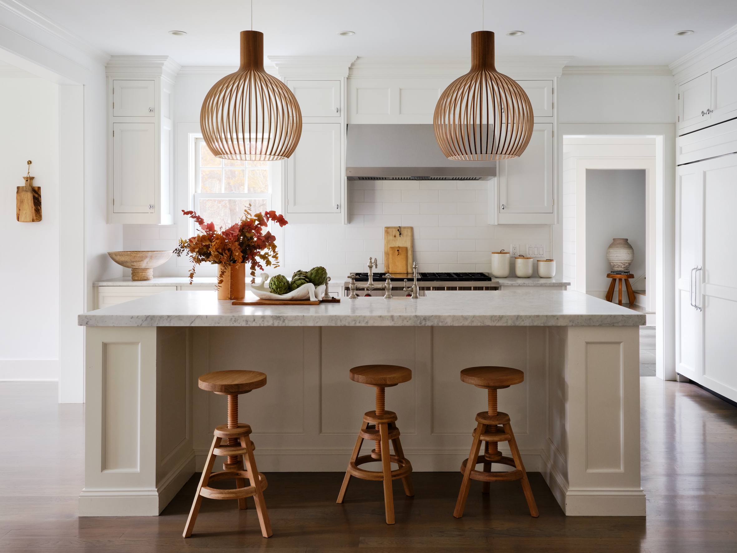 white kitchen island with 3 timber bar stools and 2 secto lamps suspended above