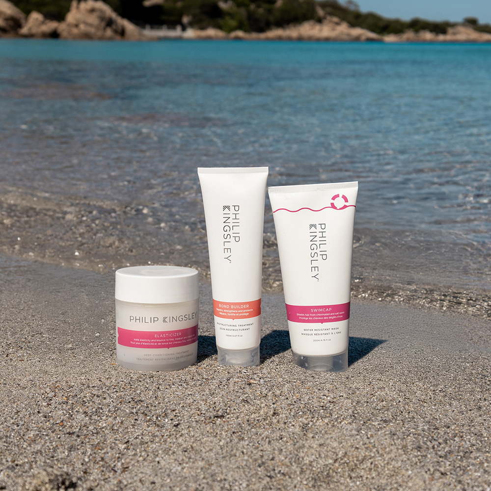 Three Philip Kingsley products on sandy beach with the sea behind them