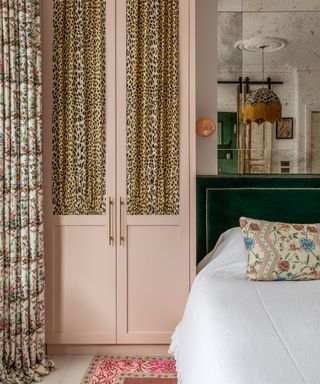 Richly textured bedroom with pink wardrobe with leopard print curtains, floral window curtains, green velvet headboard, mirrored wall,